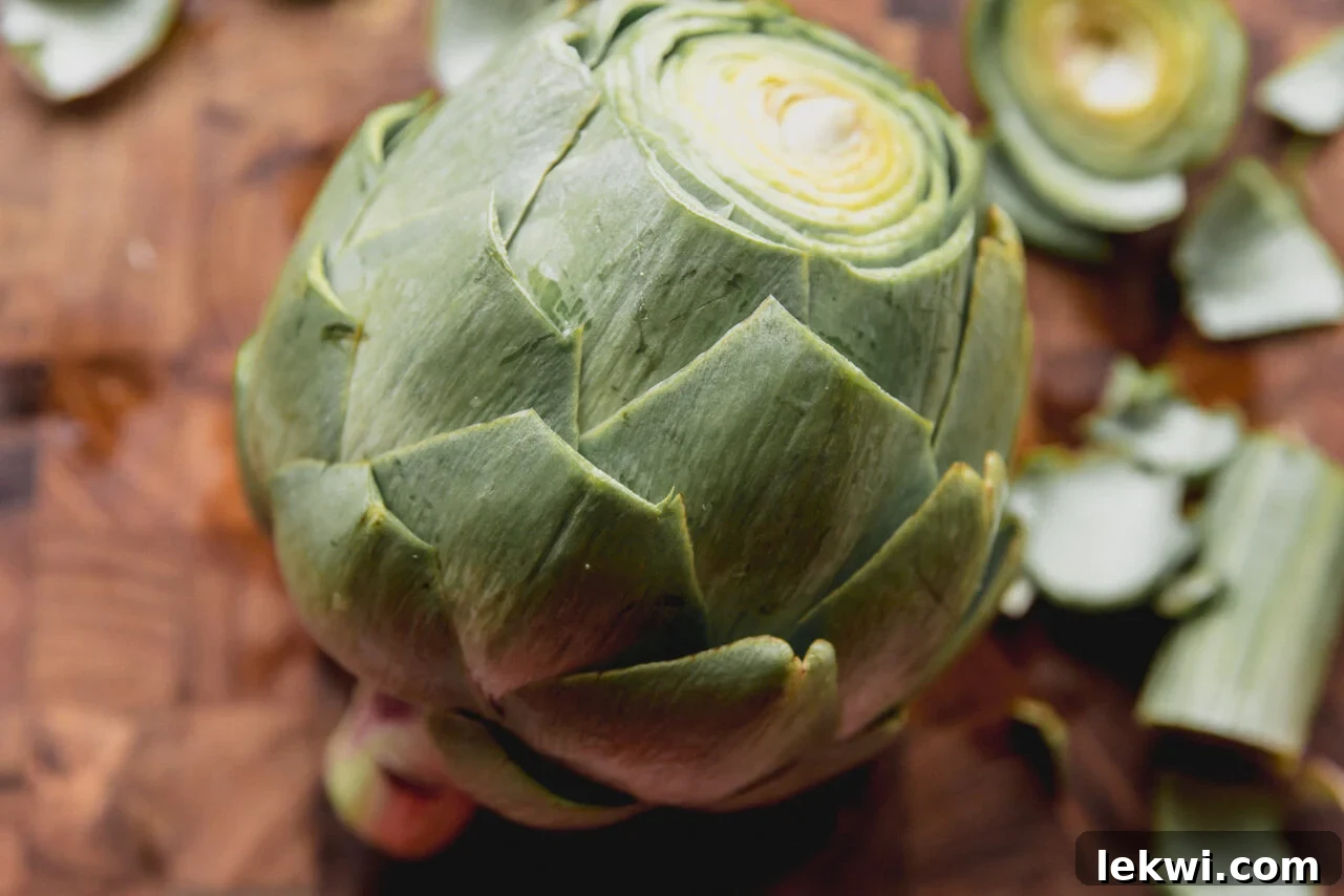 A fresh artichoke on a cutting board, with its pointed top and the tips of its outer leaves carefully trimmed, showcasing the prepared vegetable.