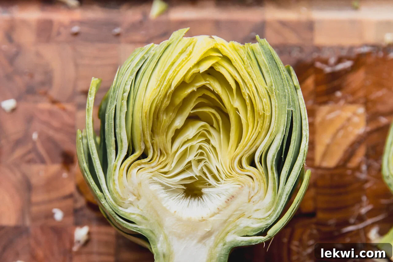 A trimmed artichoke cut precisely in half on a cutting board, revealing its interior structure and fuzzy choke.