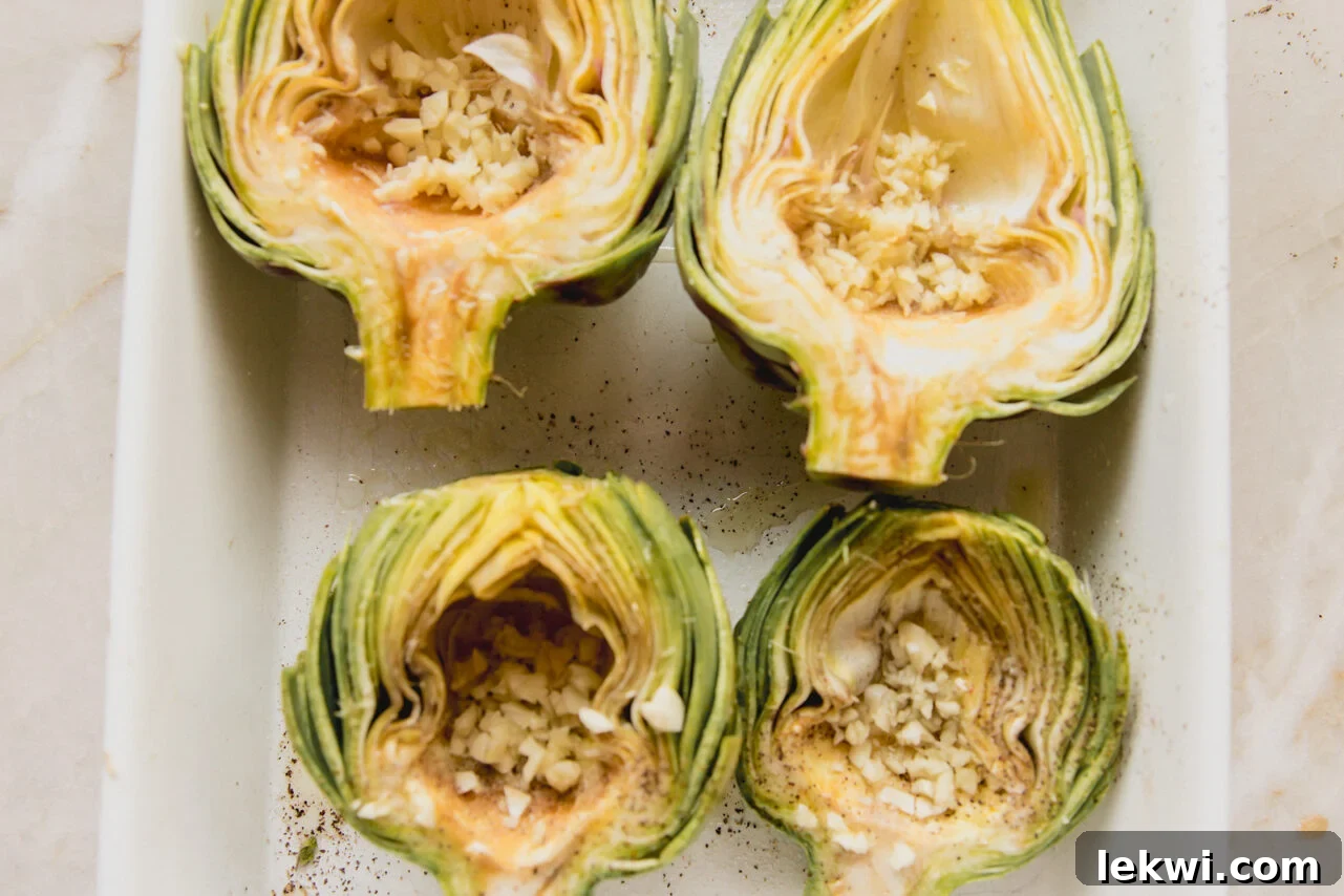 Halved and cleaned artichokes in a baking dish, generously stuffed with minced garlic cloves and drizzled with oil and seasonings.