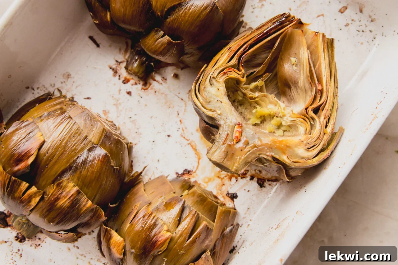 Perfectly baked artichoke halves resting in a baking dish, appearing tender and golden-brown.