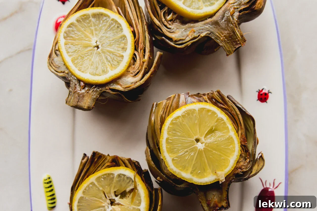 A stunning platter showcasing four oven-baked artichokes, garnished with fresh lemon slices, ready to be enjoyed.