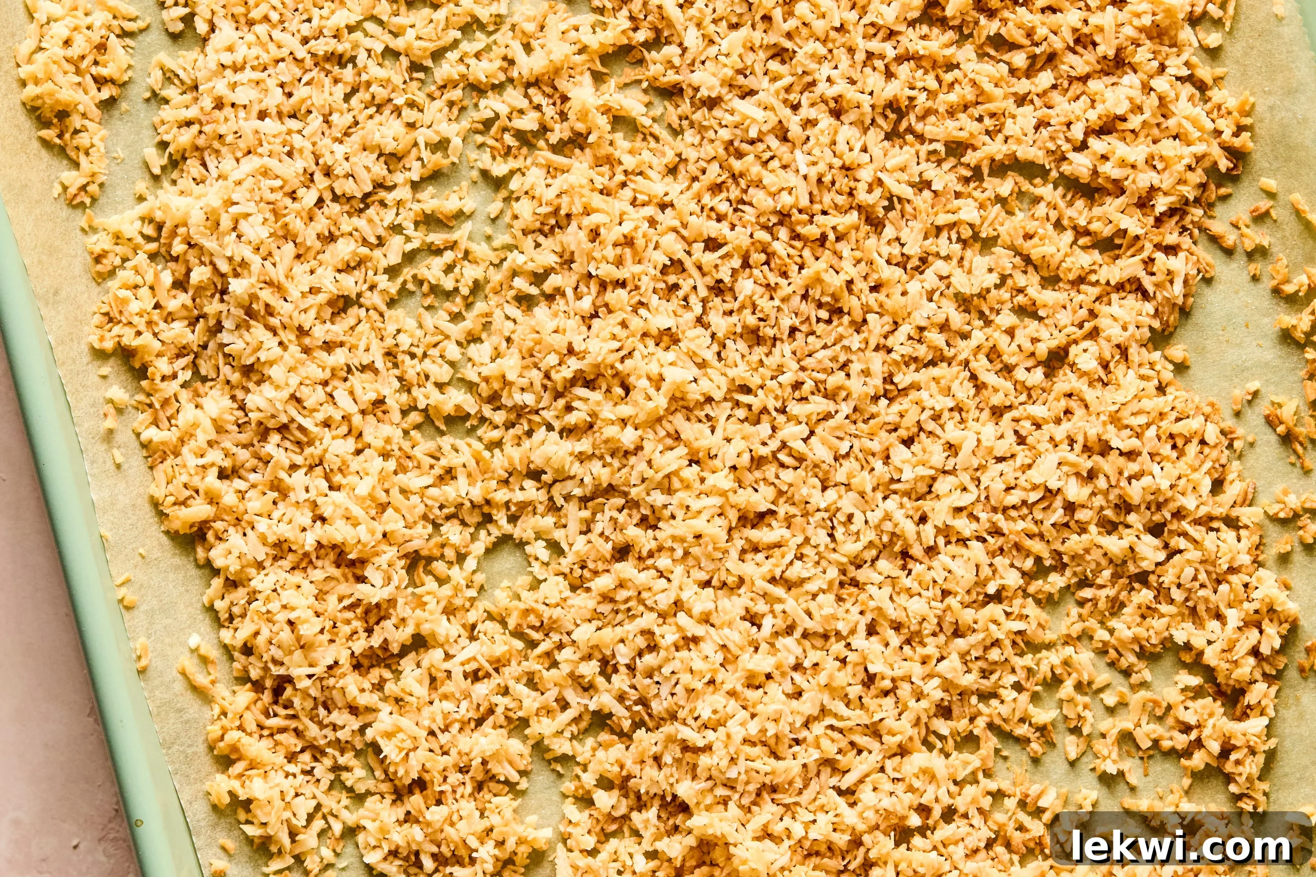 A sheet pan lined with parchment paper, holding freshly toasted shredded coconut that is golden brown and aromatic.