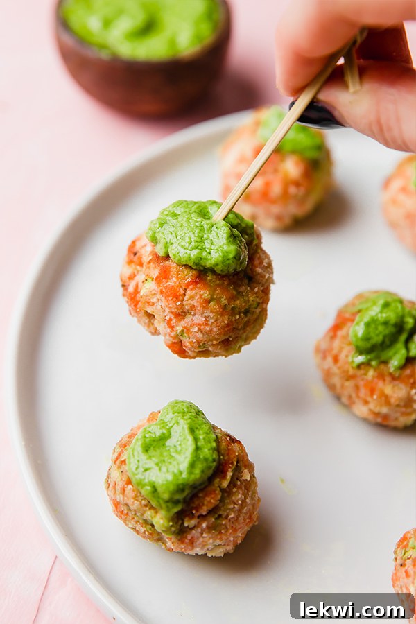 A close-up photograph captures the delectable texture of several golden-brown baked salmon meatballs, garnished with a sprinkle of fresh green herbs, enticing viewers with their appetizing appearance.