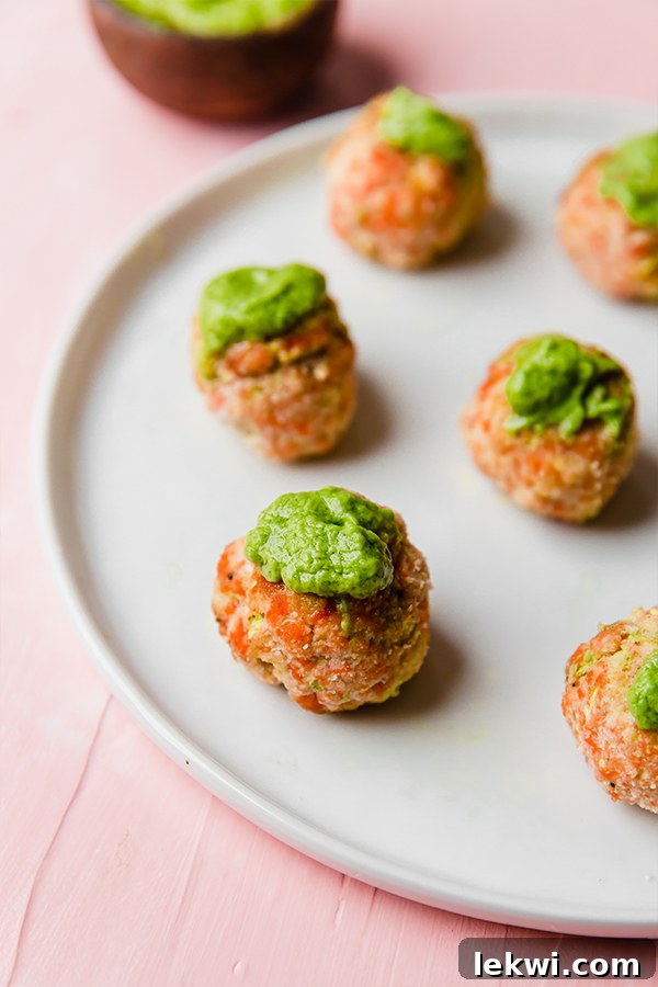 A beautifully composed arrangement of several baked salmon meatballs, perfectly golden-brown and ready to be enjoyed, with a generous serving of the vibrant green goddess sauce invitingly placed alongside for dipping.