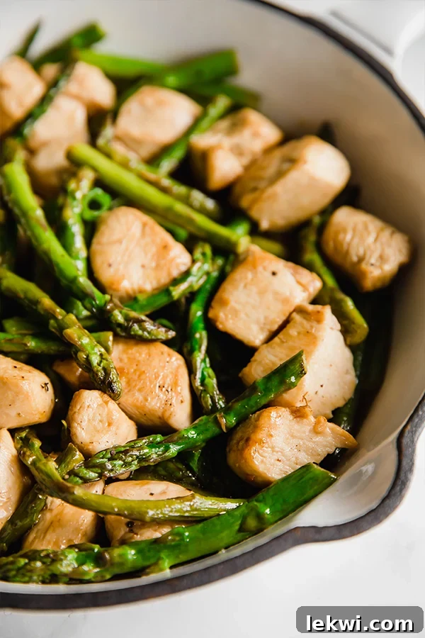A pan filled with cubed and cooked chicken and asparagus, garnished with fresh lemon slices and green onions.
