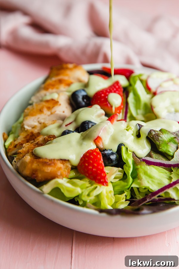 Another enticing angle of the crispy chicken salad, showcasing the golden-brown chicken tenders, vibrant mixed berries, and a generous amount of fresh green lettuce, highlighting its delectable appeal.