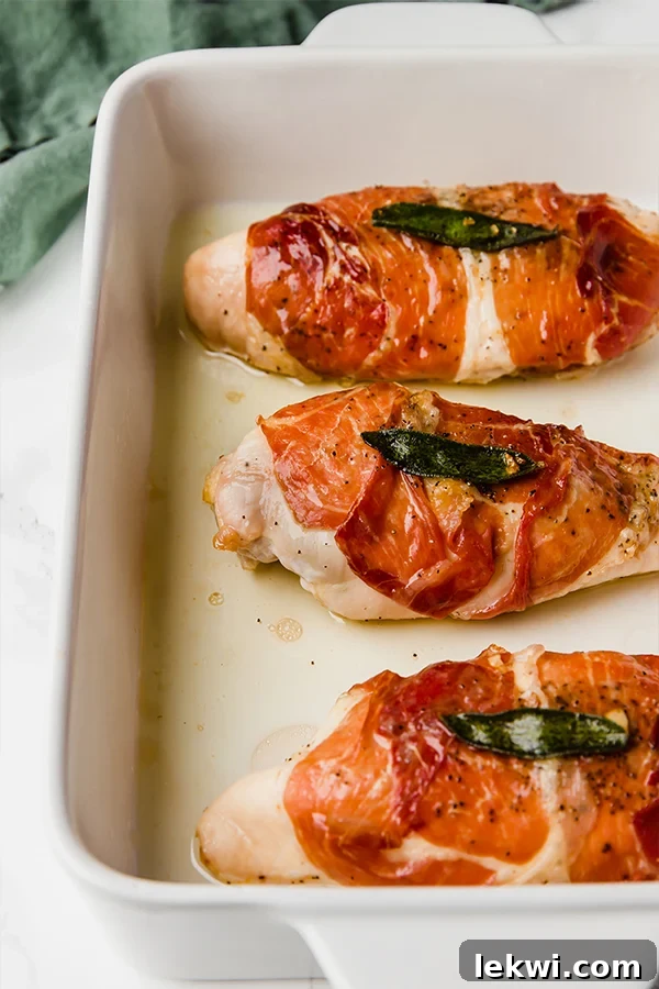 A close-up shot of baked prosciutto-wrapped chicken saltimbocca, garnished with fresh sage, on a pristine white plate.