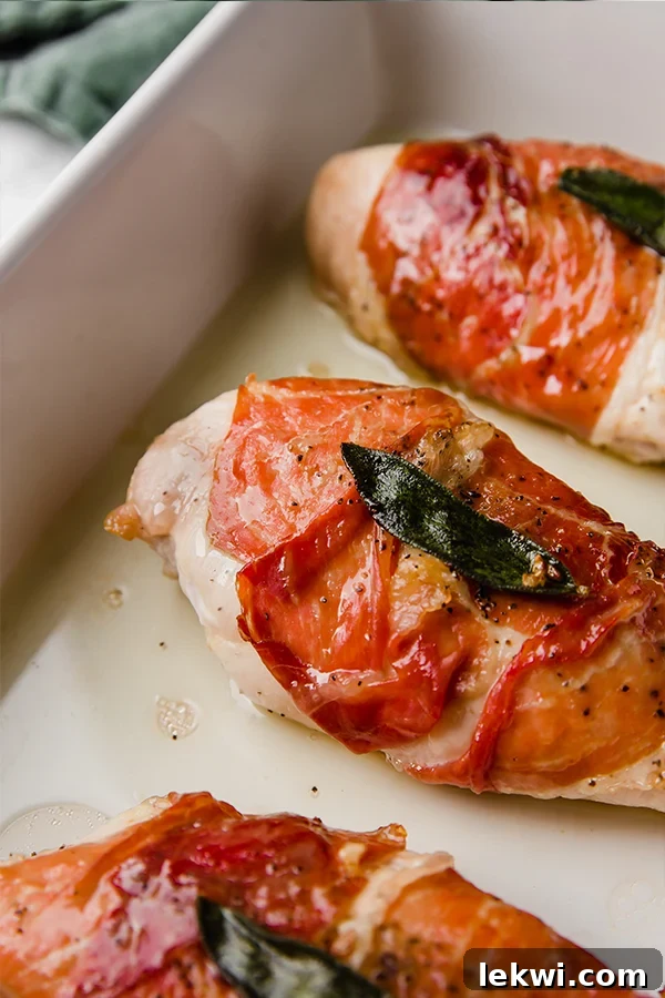 A white ceramic baking dish filled with perfectly baked pieces of prosciutto-wrapped chicken, fresh out of the oven.