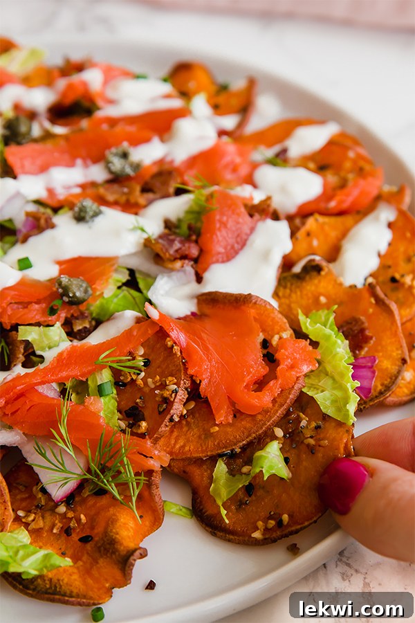 A white plate filled with everything bagel & lox breakfast nachos with a hand reaching for a bite.