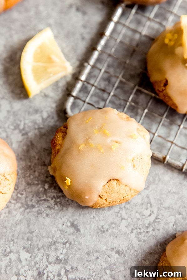 Freshly baked paleo lemon cookies on a cooling rack, glistening with a light glaze and sprinkled with lemon zest.