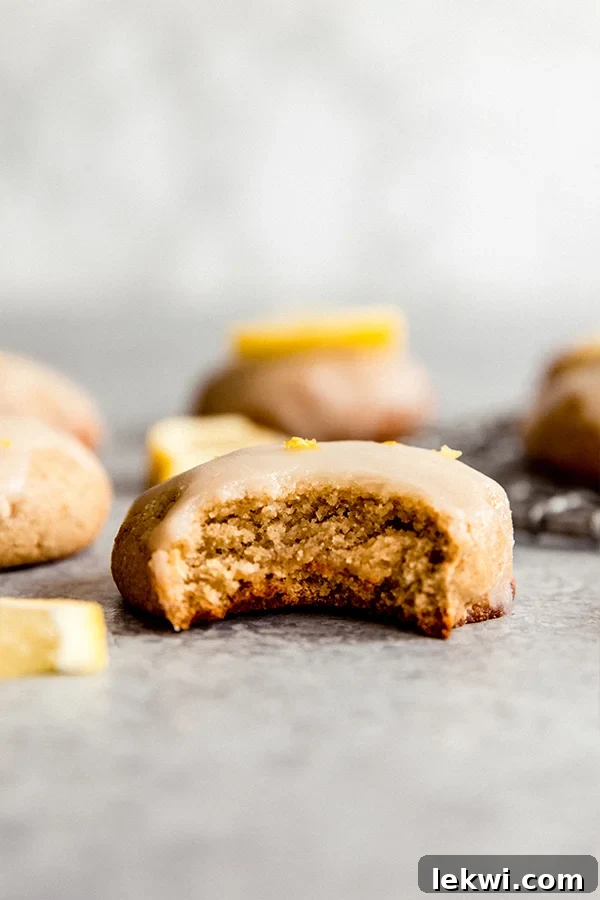 A close-up of a single paleo lemon cookie with a delicate glaze and a sprinkle of lemon zest on a white background.