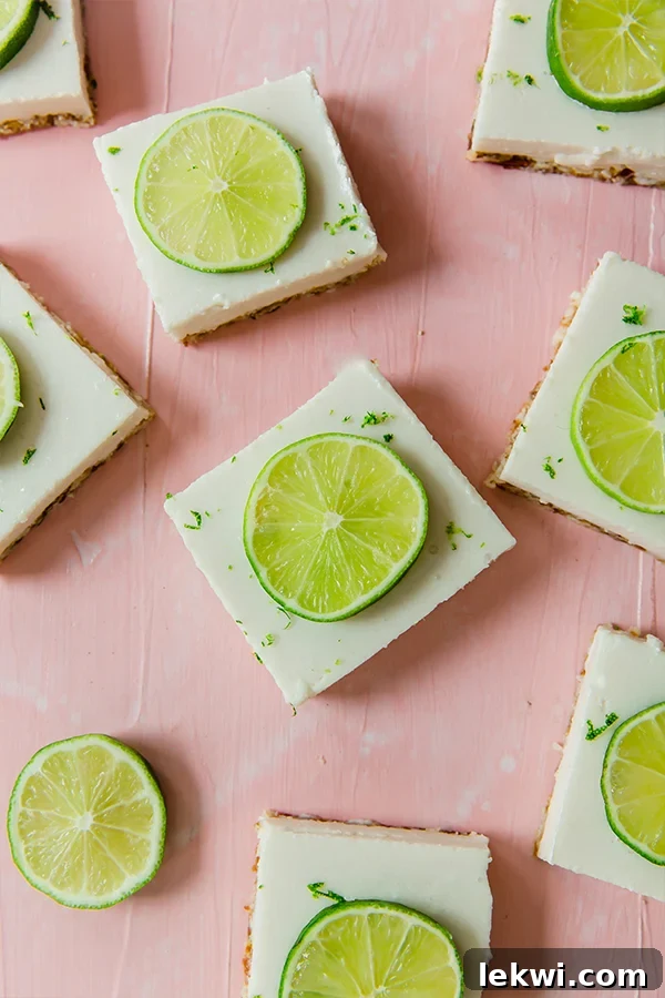 Vibrant green key lime pie bars arranged beautifully on a pink background, garnished with fresh lime wedges, highlighting their refreshing appeal.