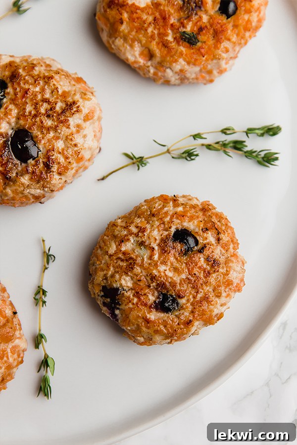 A white plate featuring plump blueberry sweet potato turkey breakfast sausages, garnished with fresh herbs.