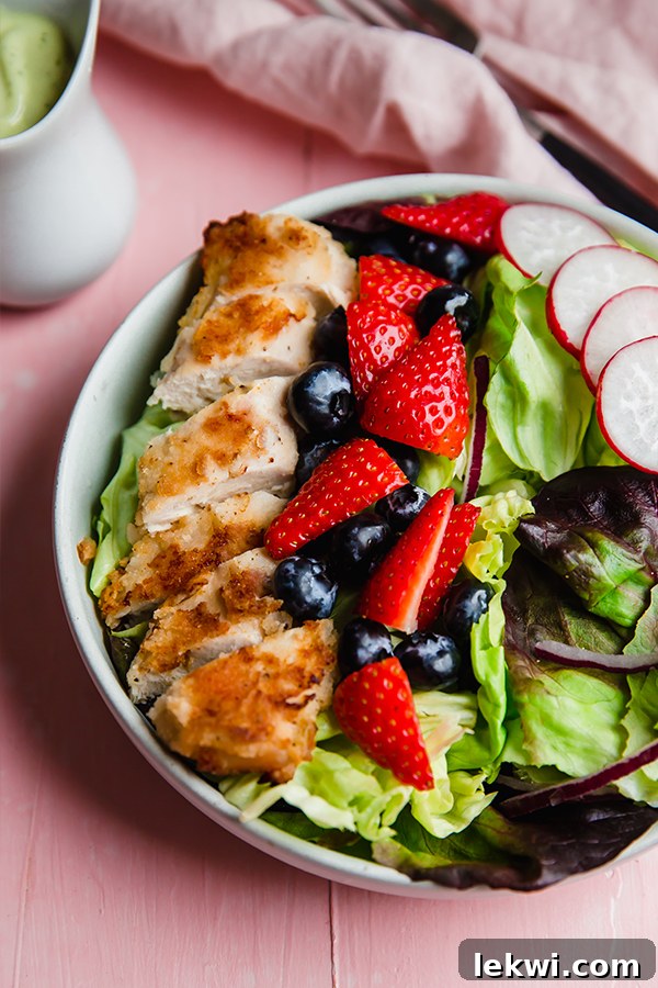 A vibrant crispy chicken salad brimming with fresh berries, radishes, and a creamy dressing.
