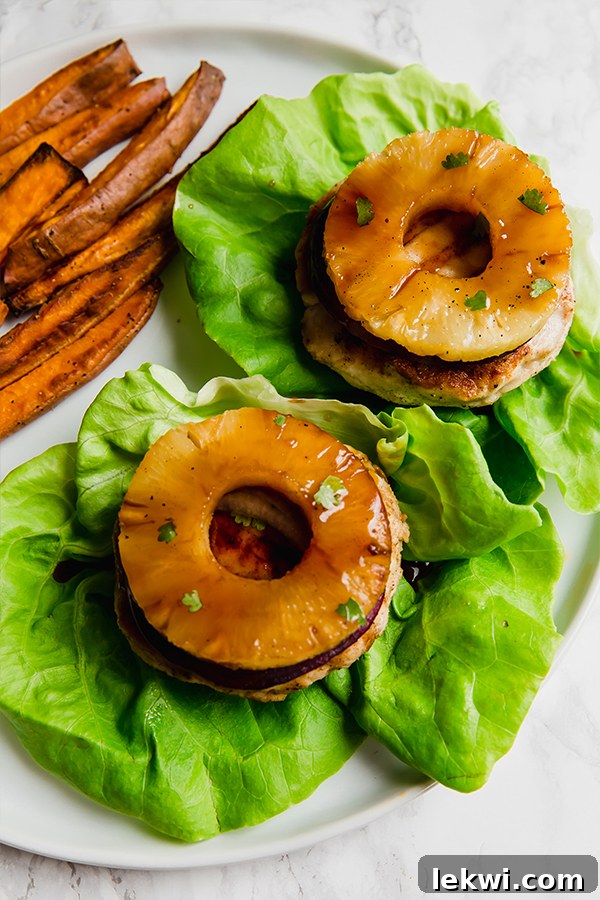 Two Hawaiian teriyaki chicken burgers topped with pineapple and on a bed of lettuce.
