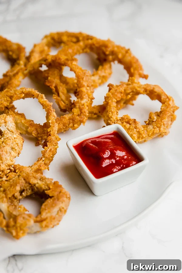 A white plate filled with perfectly golden baked onion rings next to a small bowl of dipping sauce
