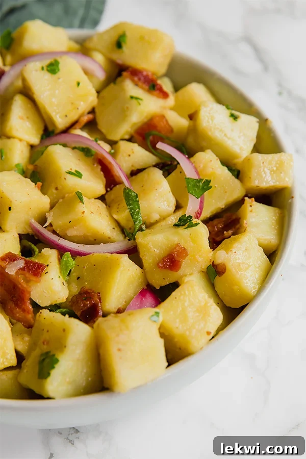 Serving bowl of no-mayo potato salad topped with crispy bacon and fresh chives.
