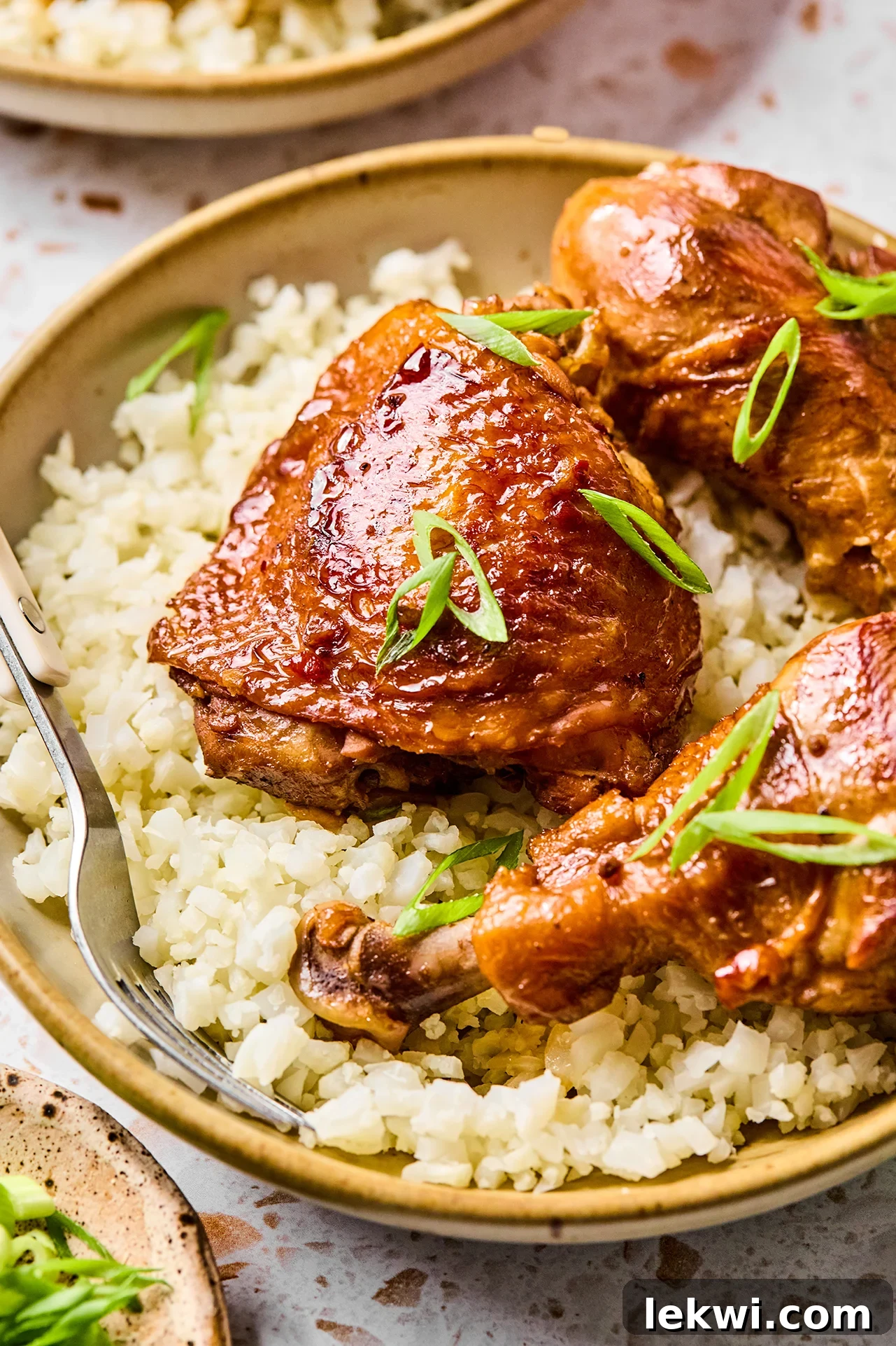 Filipino chicken adobo served over a bed of fluffy cauliflower rice, garnished with fresh green onions.