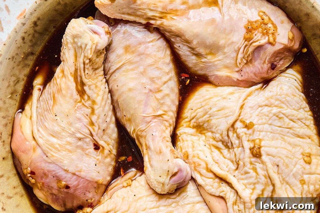 Raw chicken marinating in a bowl, covered and chilling in the refrigerator.
