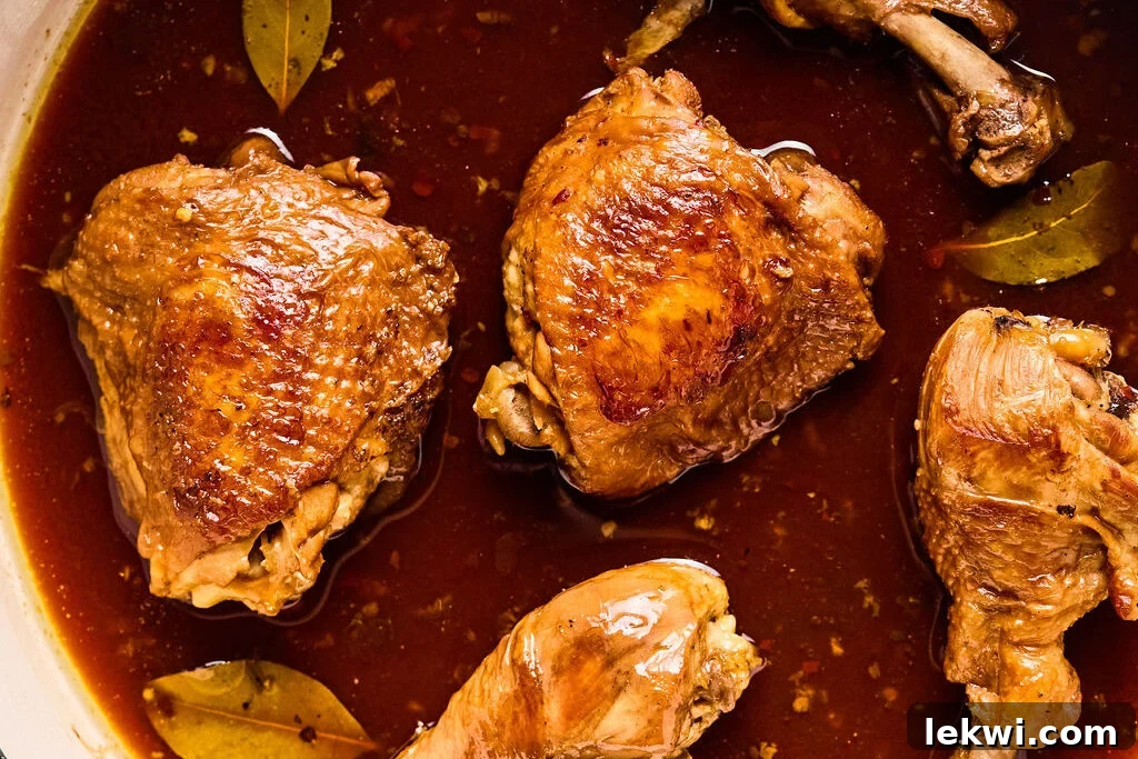 The chicken simmering in the rich Adobo sauce with bay leaves in a pan.