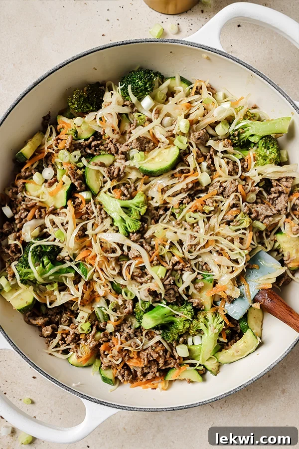 A large skillet filled with ground beef and cabbage stir fry, garnished with fresh green onions, ready to be served.