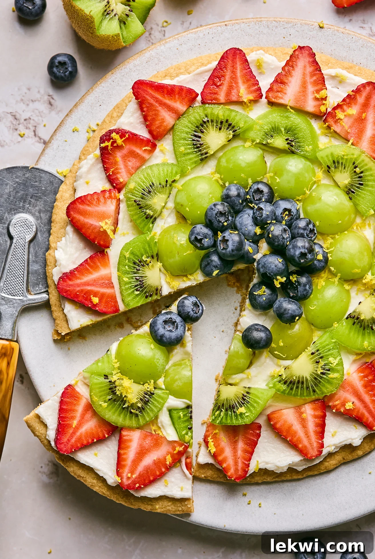 A sugar cookie fruit pizza on a platter with one slice being cut out.