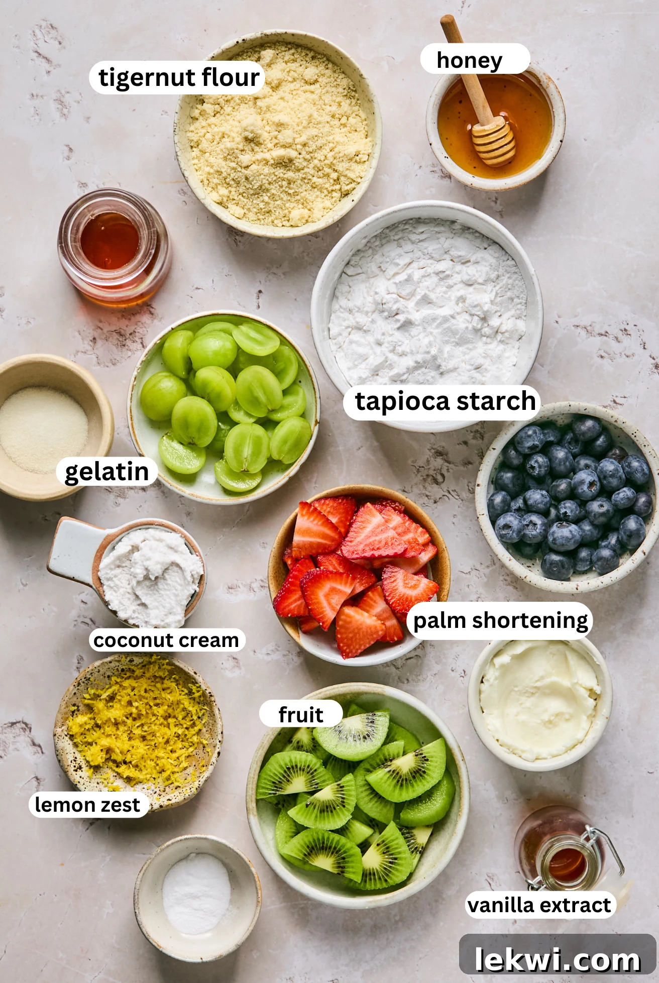 Individual bowls holding all the ingredients for the sugar cookie fruit pizza crust and frosting, including flours, shortening, coconut cream, and fresh fruits.