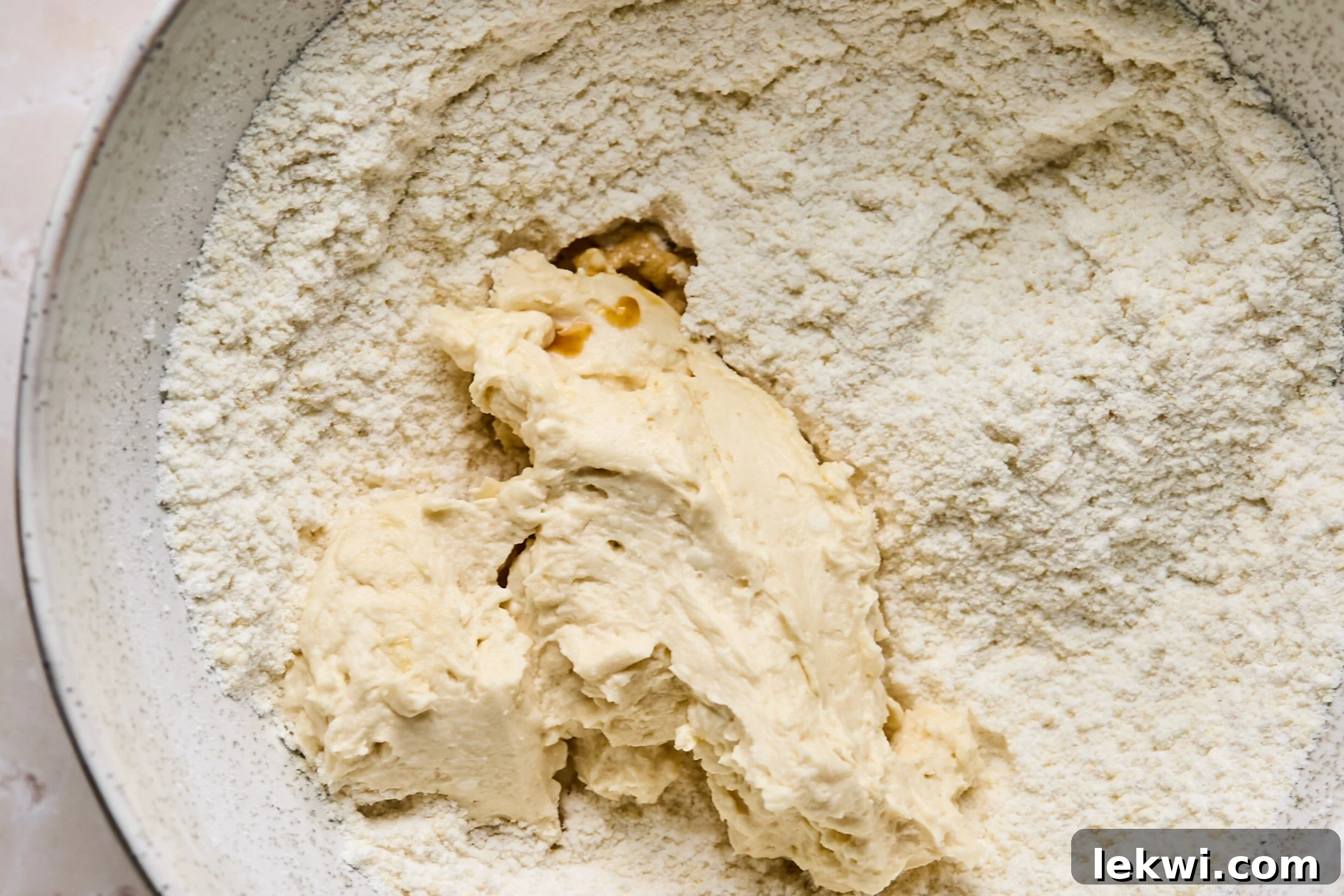 A bowl of wet ingredients, primarily a creamy, light-colored mixture, being mixed vigorously, forming the base for the sugar cookie pizza dough.