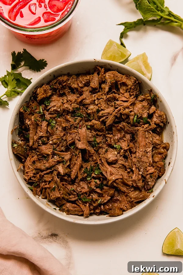 Bowl of barbacoa beef garnished with fresh cilantro and lime wedges, ready to be served.