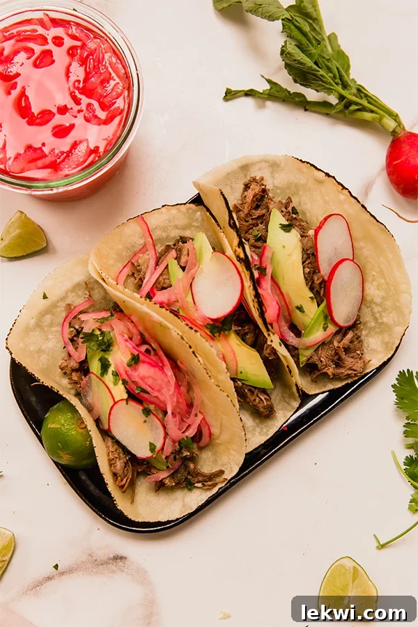 Plate with several barbacoa beef tacos, topped with cilantro and pickled onions.