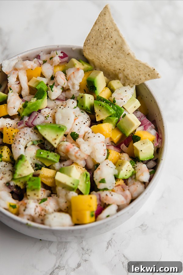 A white bowl filled with vibrant mango shrimp ceviche, with a single plantain chip dipped in, ready to be enjoyed.
