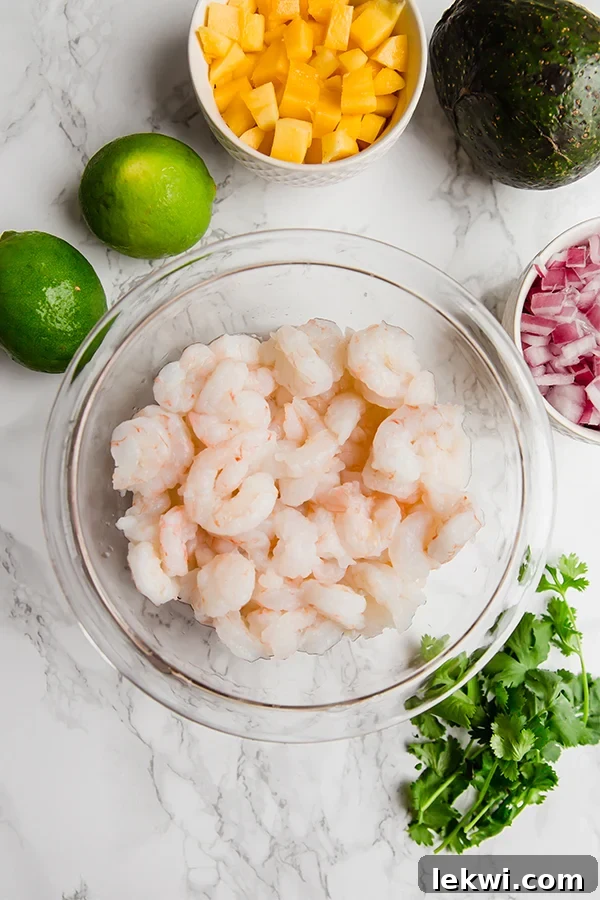 A vibrant collection of raw shrimp, red onions, fresh cilantro, and halved limes arranged artfully in a glass bowl.