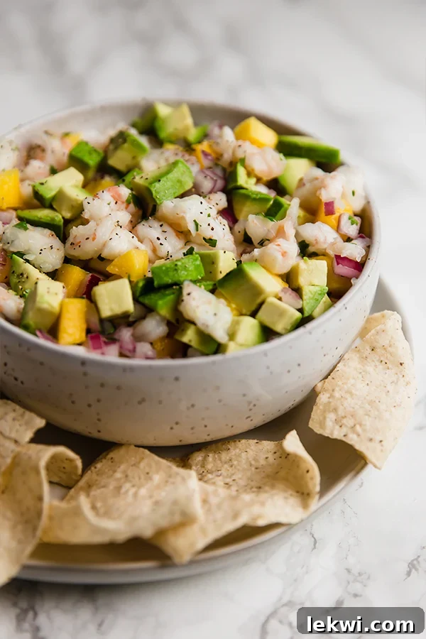 A white bowl filled with vibrant mango shrimp ceviche, surrounded by crispy tortilla chips ready for dipping.