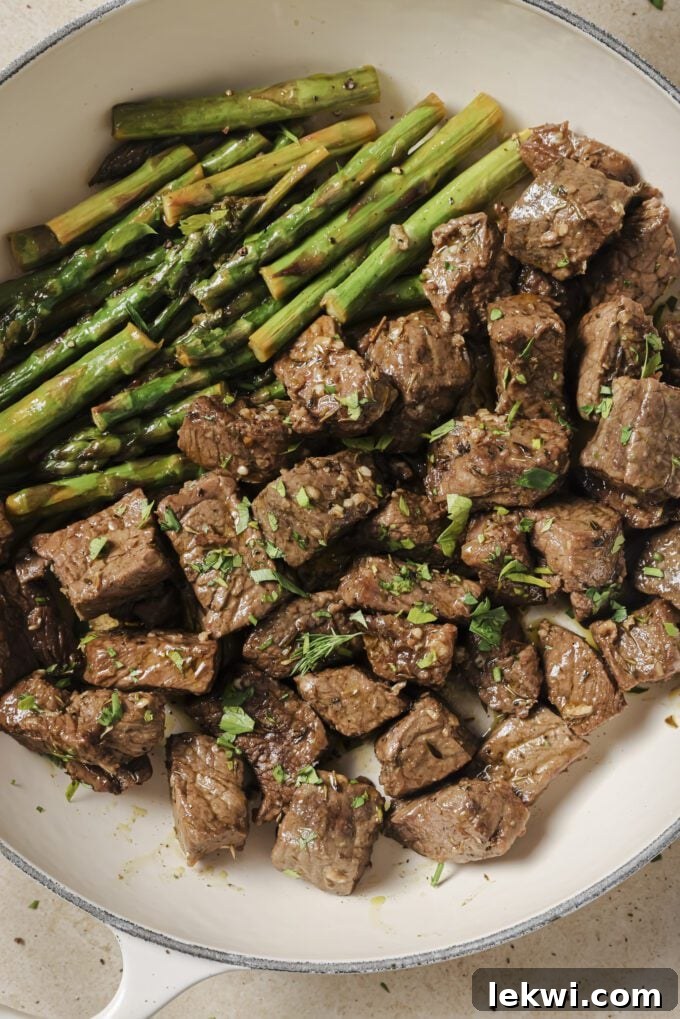 Garlic and balsamic steak bites with asparagus topped with parsley in a white pan.