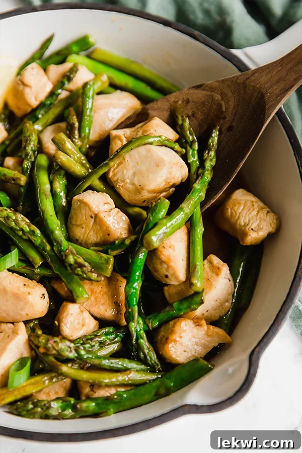 A pot with cooked, cubed chicken and asparagus with a wooden spoon serving some.