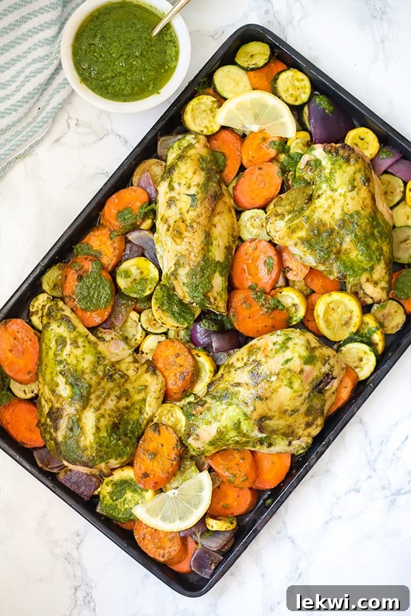 A sheet pan with cut out squash and carrots and chicken topped with pesto to make one pan pesto chicken.