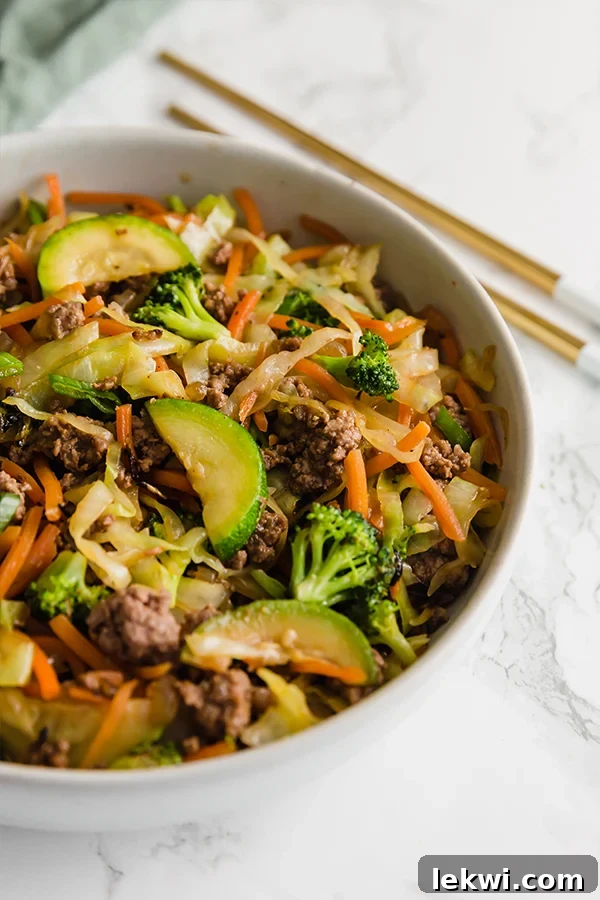 A white bowl filled with ground beef stir fry and chop sticks next to the bowl.