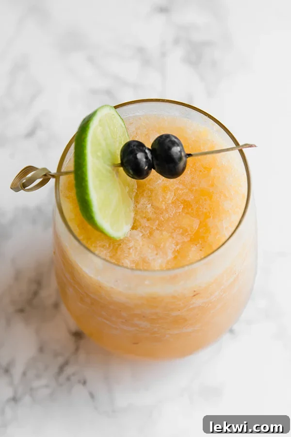 A frosty glass of peach bellini mocktail garnished with a vibrant lime wedge and fresh blueberries, ready to be enjoyed on a sunny day.