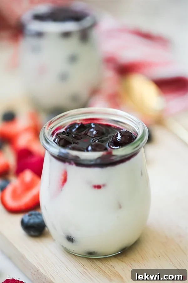 A glass jar filled with layers of red, white, and blue panna cotta, topped with fresh berries.