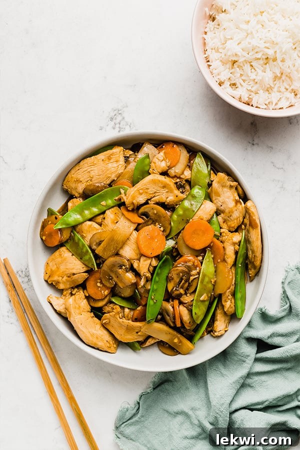 Chopsticks picking up a piece of chicken from a plate of Moo Goo Gai Pan, highlighting the fresh ingredients.