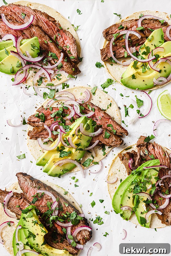 Several carne asada tacos with avocado and red onion.