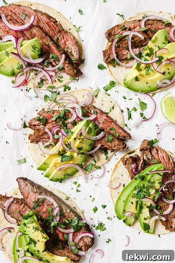 Several carne asada tacos with avocado and red onion.