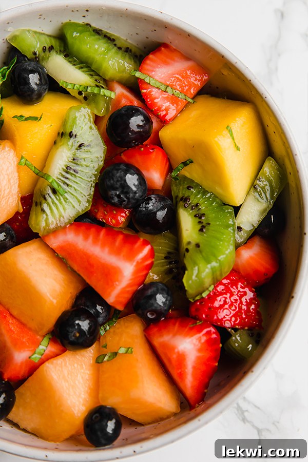 Colorful and inviting fruit salad in a large glass bowl, garnished with mint