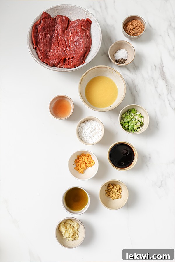 A collection of Orange Beef ingredients, including sliced flank steak, fresh garlic, ginger, orange halves, coconut aminos, and arrowroot starch, displayed in separate bowls.