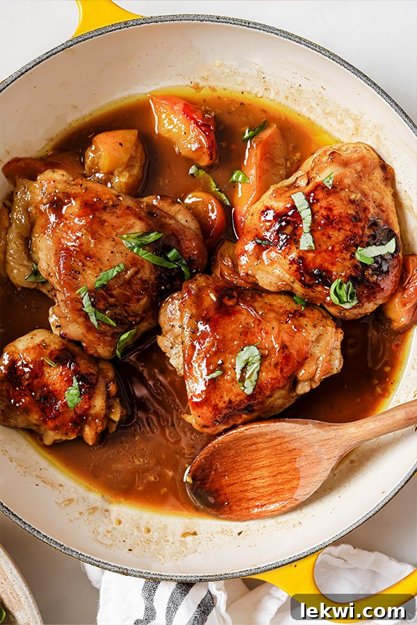 One pan balsamic peach chicken thighs topped with fresh basil in a yellow pan with a wooden spoon, ready to be served.