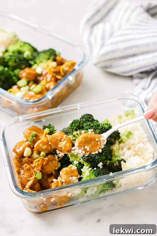A person holding a fork with a bite of homemade orange chicken, highlighting its deliciousness.