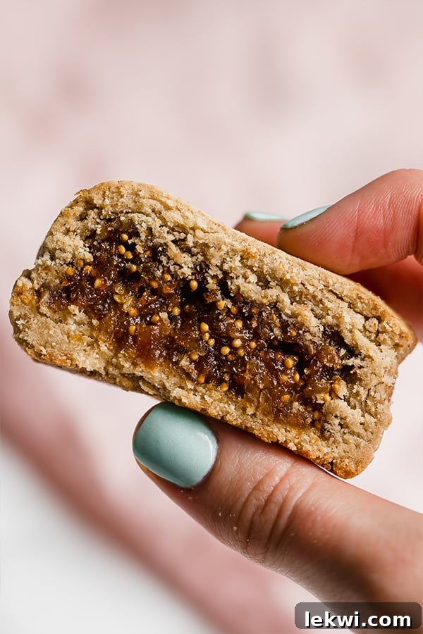 A hand holding a perfectly baked, golden-brown homemade Paleo Fig Newton, showcasing its crumbly texture and delicious fig filling.