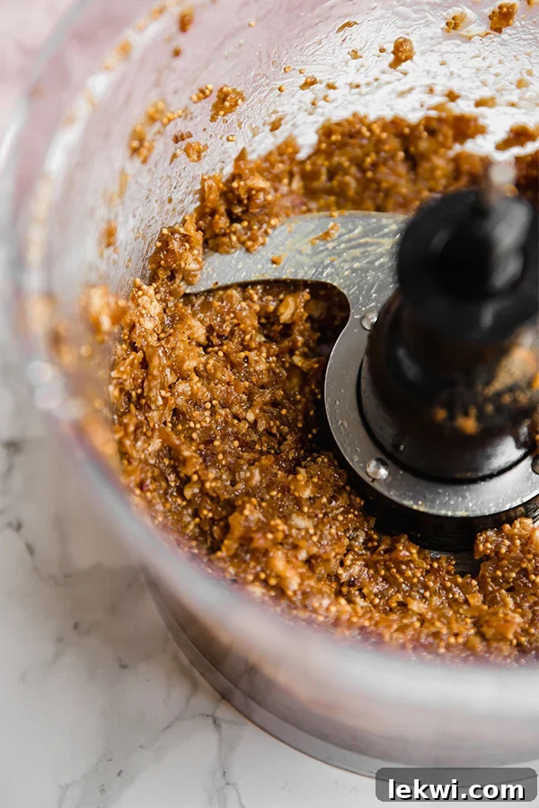 A close-up of the smooth, dark, and sticky fig filling mixture in a food processor, ready to be spread into the cookie dough.