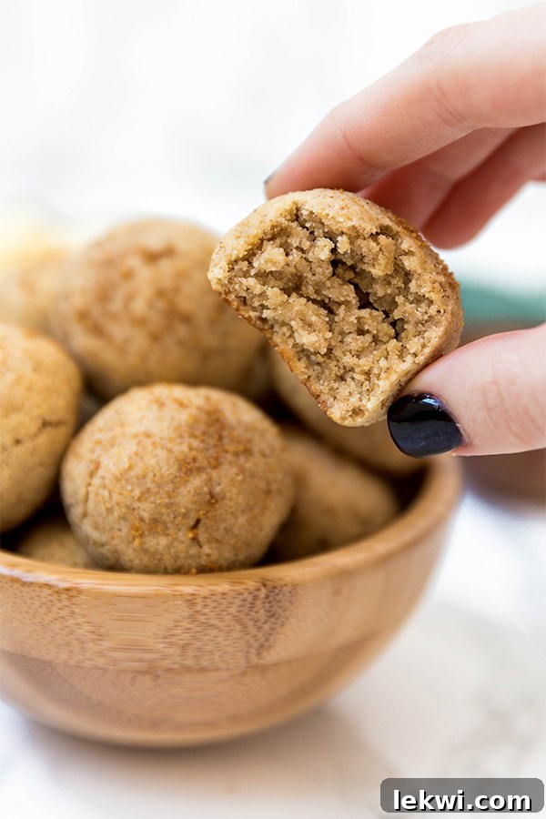A hand gently reaching into a rustic wooden bowl filled with freshly baked apple cinnamon sugar donut holes, capturing a moment of sweet indulgence.
