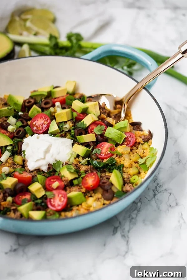 A rustic serving dish brimming with a flavorful one-pan taco skillet, beautifully garnished with fresh avocado slices and a dollop of creamy coconut cream, ready to serve.